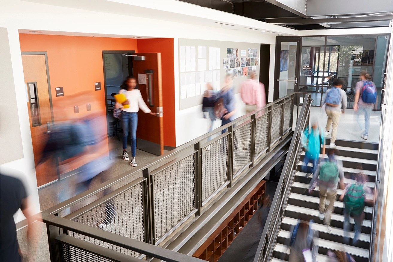 Ansicht eines Treppenhauses in einem modernen Schulgebäude mit vielen Schülern die gerade in Bewegung sind.